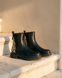 Paire de boots Chelsea AGATHE noires posée sur une marche en pierre — A by André