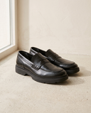 Mocassin ARCHIBALD noir posé sur sol béton clair, mur enduit crème