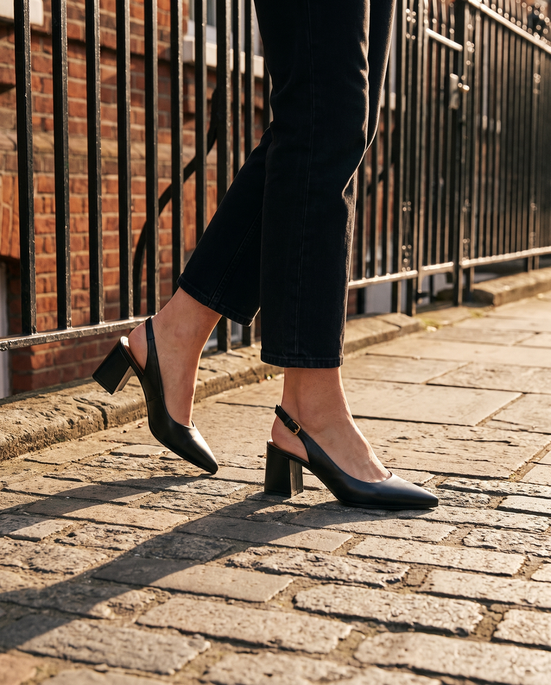 Slingback JULIE noire portée, gros plan, sur les pavés d'une rue londonienne